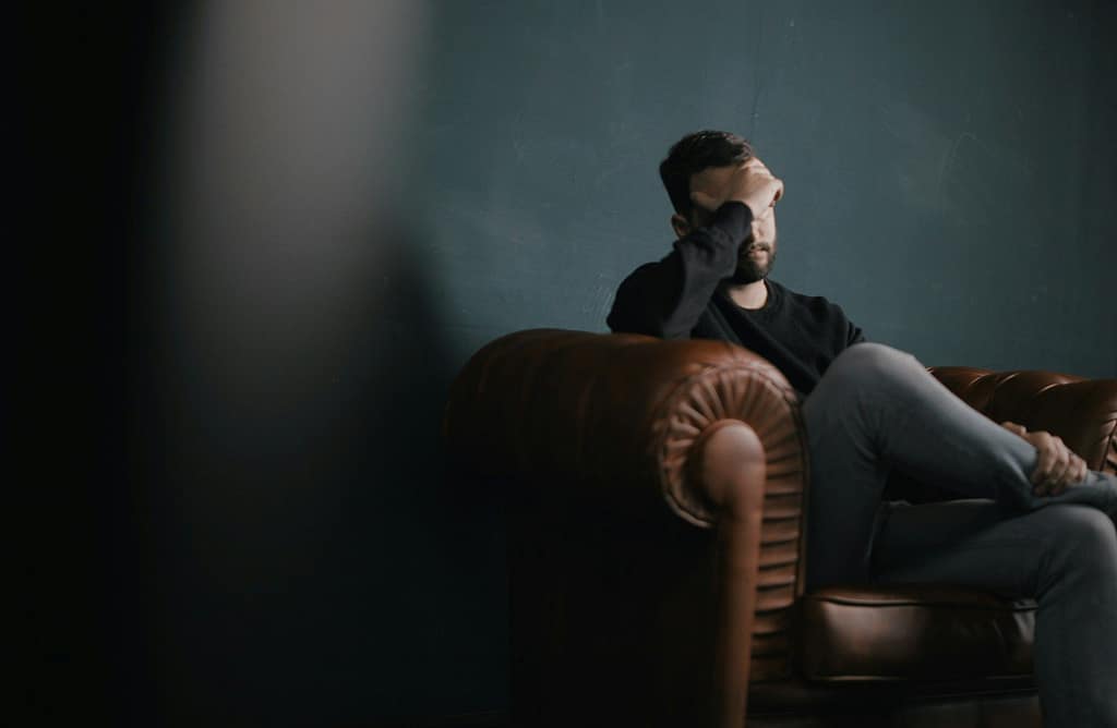 a man holds his head while sitting on a sofa - ADHD Depression