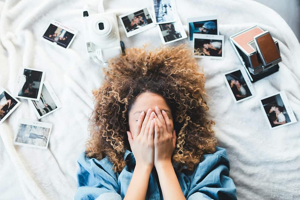 woman lying on bed covering her face surrounded by photos and white camera. does adhd affect memory