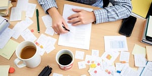 Person at desk with notes and coffee, focused on work.