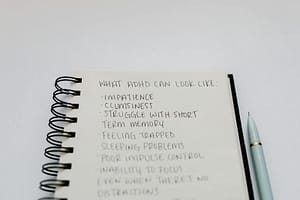 Photo by Tara Winstead - Philanthropeak Coaching A notebook with handwritten ADHD symptoms like impatience and focus issues.