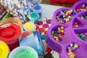 Colorful craft supplies including beads and paints - Philanthropeak Coaching pink plastic toy on white table. ADHD toys adults