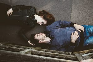 Couple lying on the ground, looking affectionately. - Philanthropeak Coaching man and woman lying on gray concrete surface looking at each other - living with a partner with ADHD